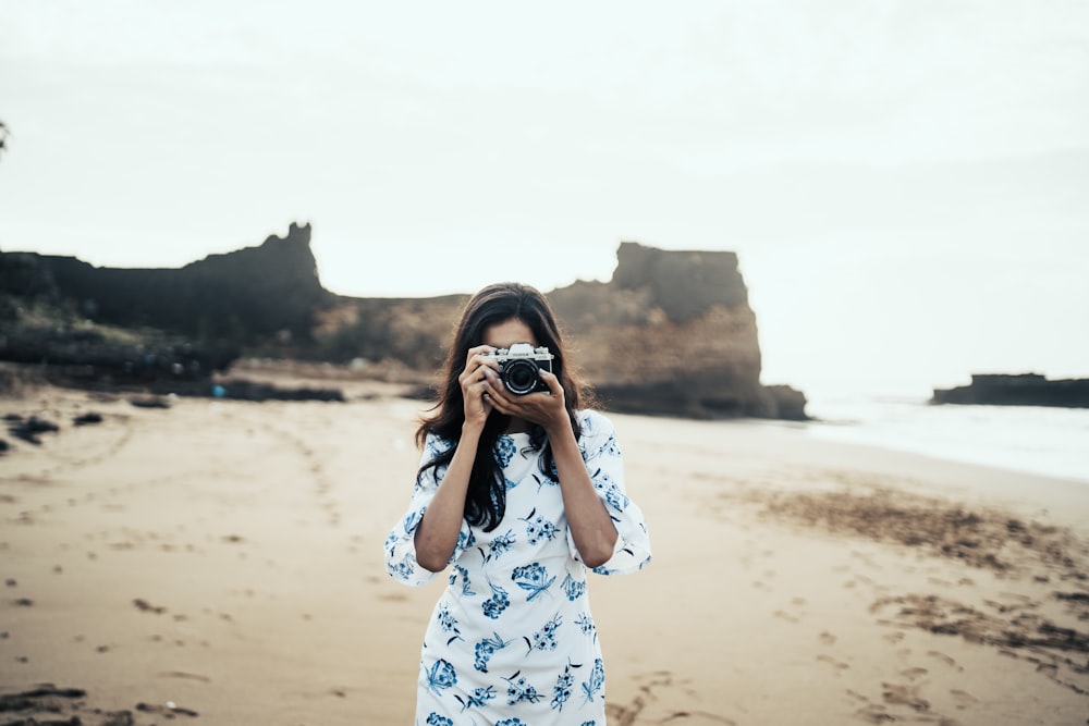 femme portant une robe à fleurs blanche et bleue tenant un appareil photo noir et gris