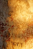 Close-up of a textured wall with faded graffiti and subtle earth tones under soft natural light.