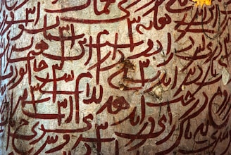 Intricate Arabic calligraphy in deep red is etched onto a textured stone surface. The script is decorative and flowing, creating a sense of artistic expression and cultural heritage.