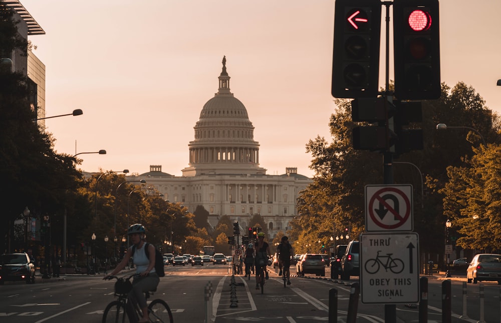 Menschen, die auf der Straße Fahrrad fahren, und verschiedene Fahrzeuge, die das Kapitol der Vereinigten Staaten während des Tages betrachten Screenshot