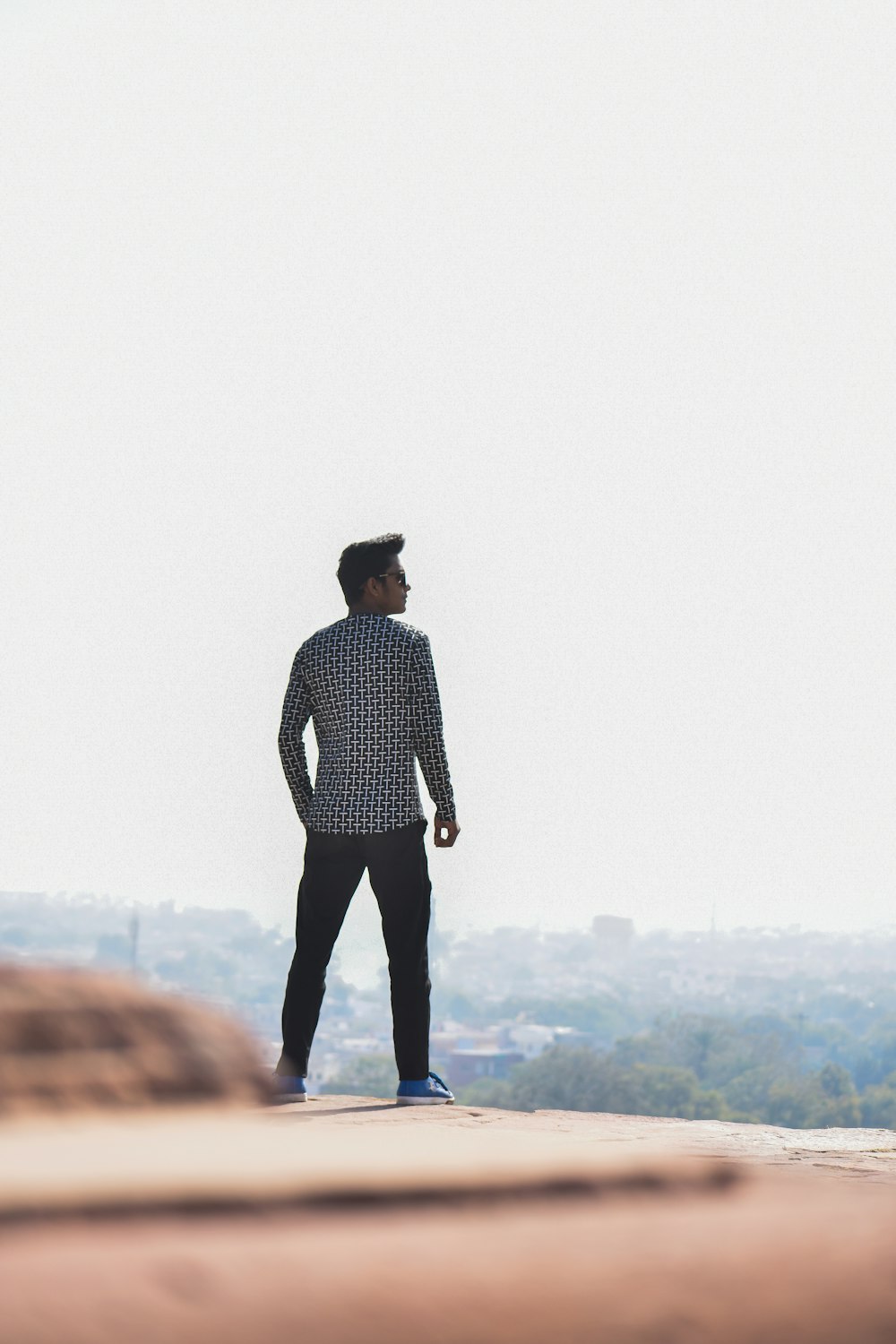 man wearing white and black long-sleeved shirt standing on rocky hill during daytime