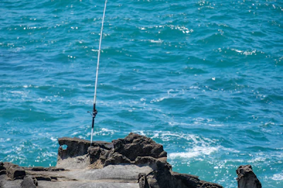 Angler adjusting fishing rig with turquoise water and sandy beach in the background.