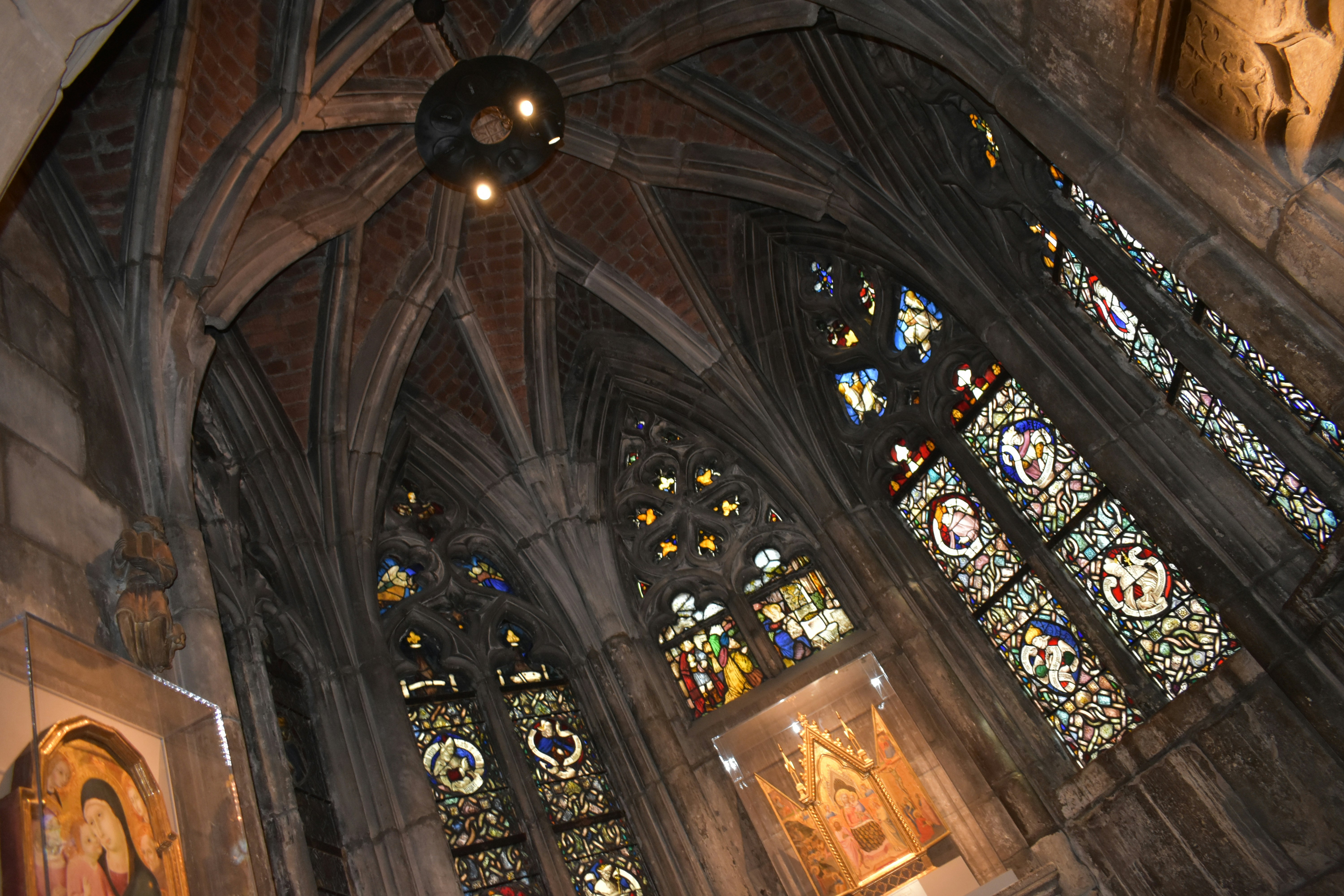 Interior de catedral gótica con luz que entra por vitrales de colores, ambiente solemne y oscuro de piedra antigua