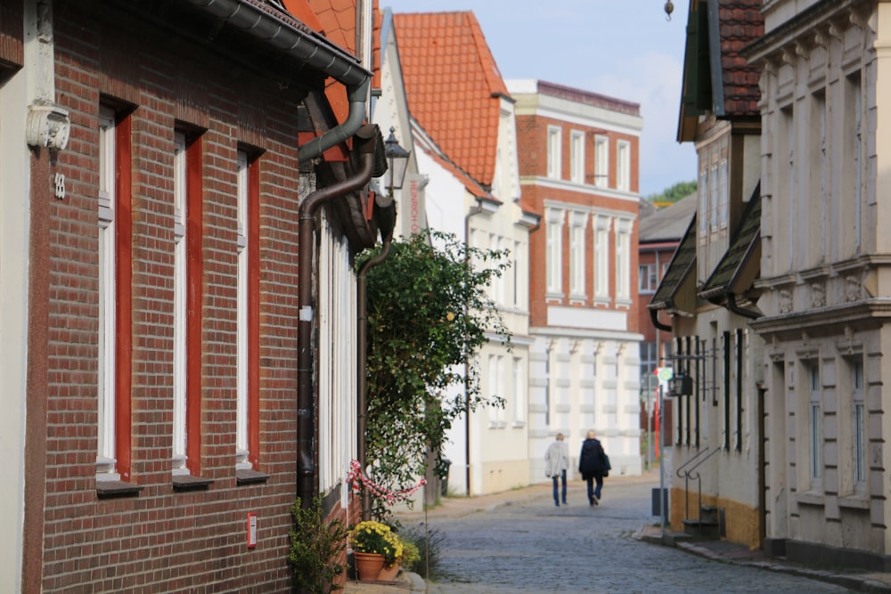 two people walking on concrete road in between buildings during daytime