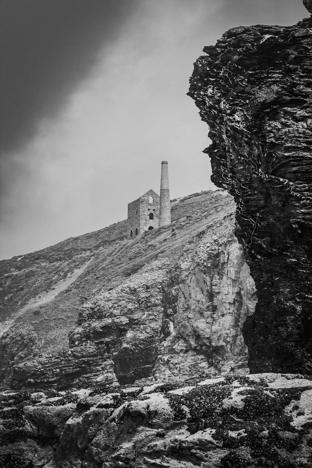 grayscale photography of house on hill near big rock formation