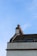 A rooftop with a row of decorative brick chimney pots set against a clear blue sky. The roof is slanted and covered in wooden or slate shingles. Part of a window is also visible beneath the roofline.