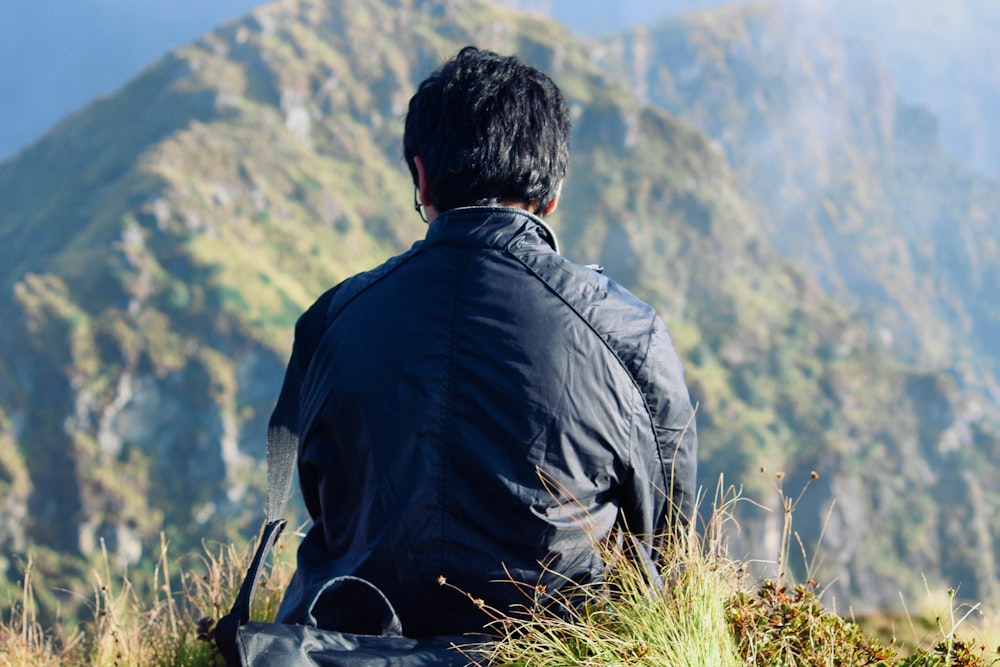 Mann sitzt auf Klippe und trägt blaue Jacke