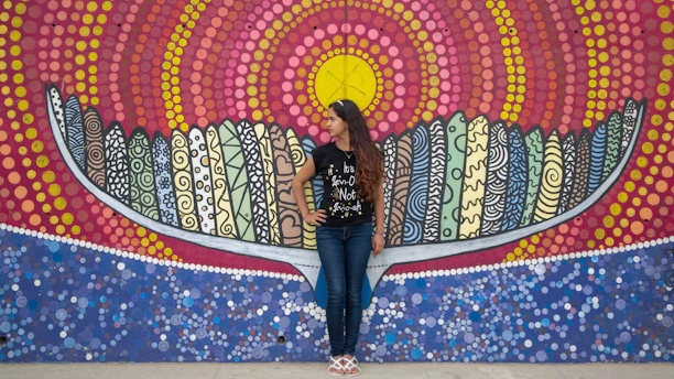 A vibrant young woman wearing a colorful short kurti, standing against a bright urban mural.