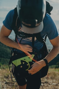 A close-up of hands adjusting a sturdy backpack strap against a backdrop of a sunlit mountain trail.
