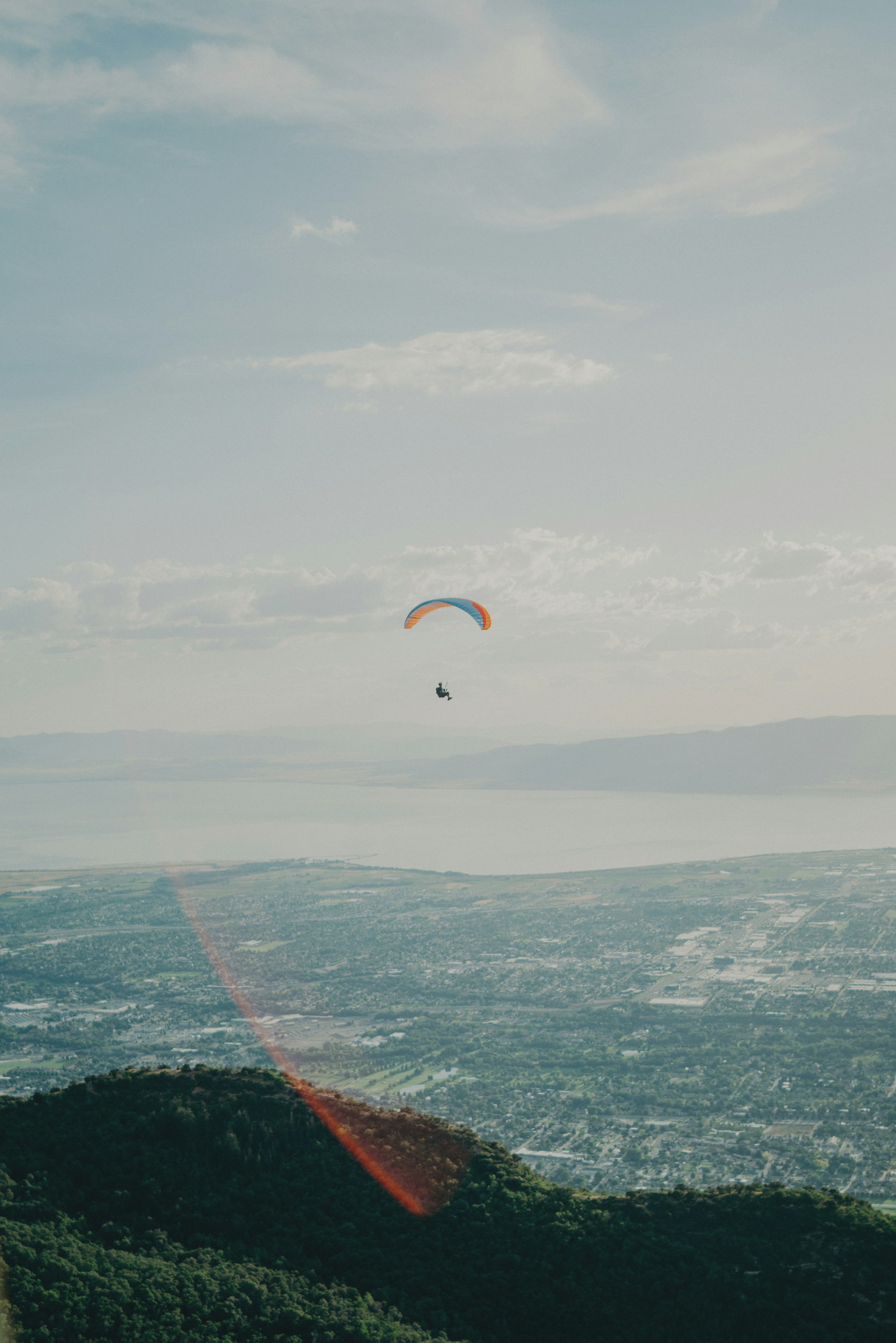 A tandem paraglider soaring above the Cerro Arco with the city of Mendoza and the precordillera mountains in the background under a clear blue sky.