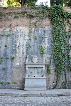 A charming stone fountain with moss-covered walls near a walking path.