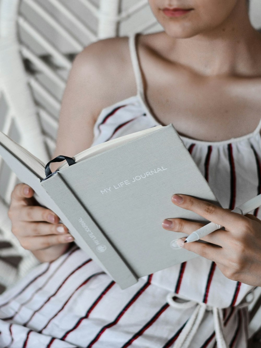 Donna che legge il libro mentre è seduta sulla sedia bianca