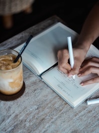 A close-up of a person writing creative email content on a notepad beside a coffee cup.