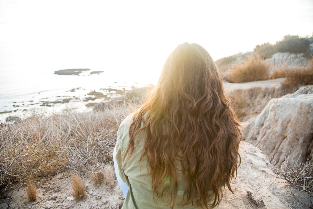 person sitting and facing near body of water during daytime