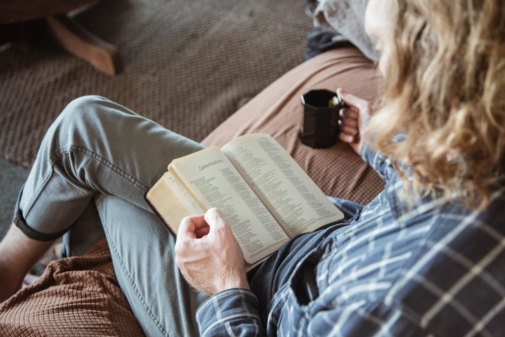 person holding book and black ceramic mug close-up photography