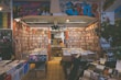 A cozy music store filled with vinyl records and DVDs, featuring colorful graffiti on the walls. Shelves are lined with a vast collection of CDs and records in an organized manner. Soft lighting adds to the inviting atmosphere, and a few customers are browsing the selection.