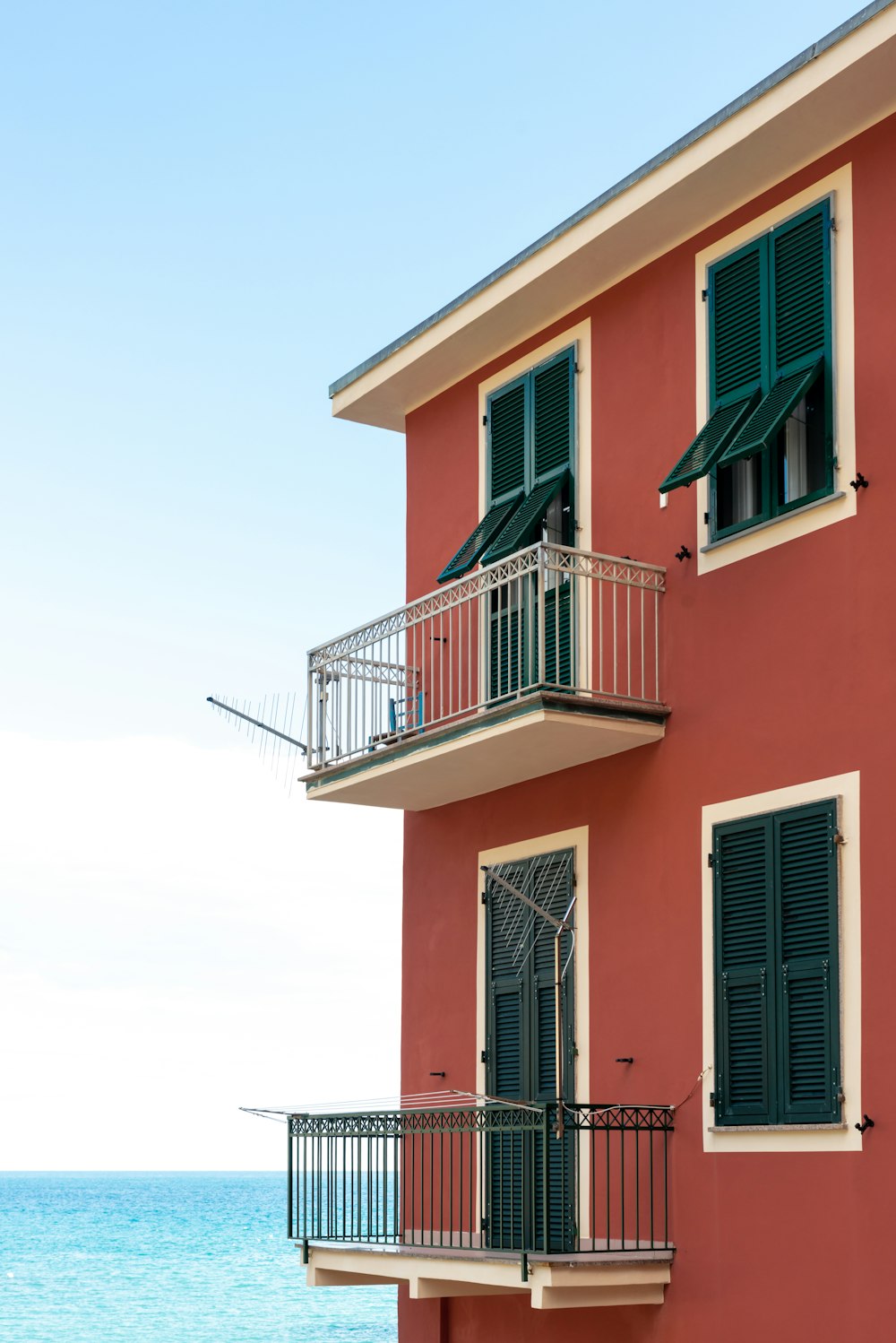 a red building with green shutters next to the ocean