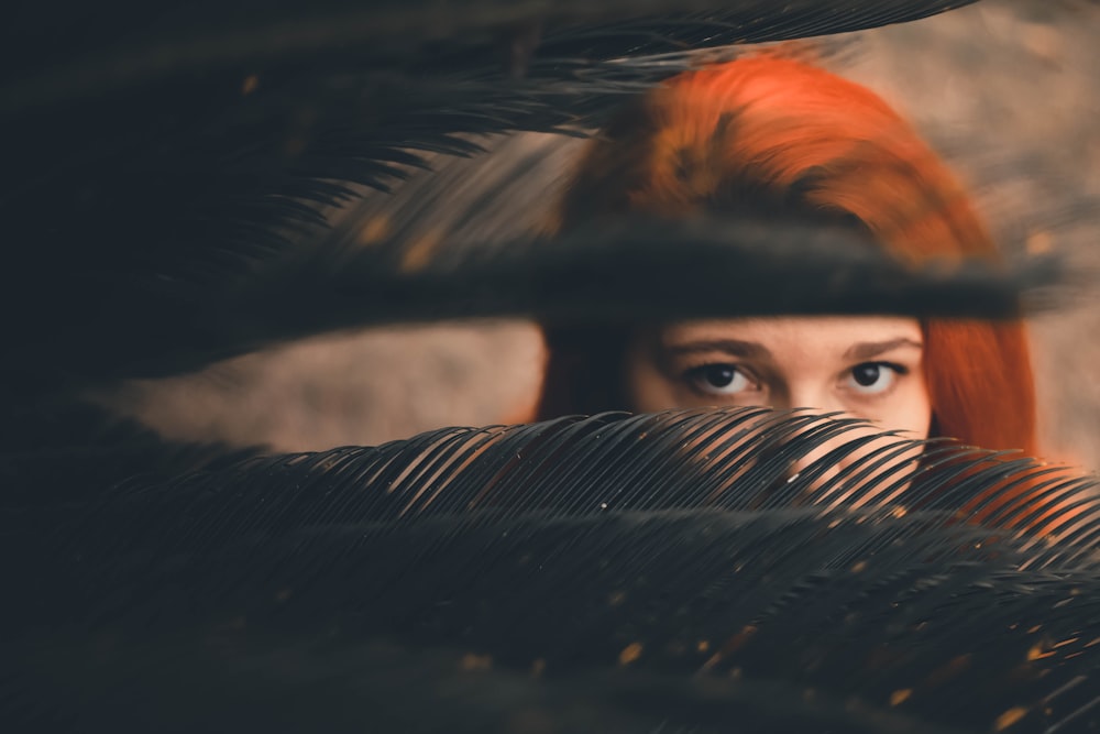 a woman with red hair looking out from behind a palm tree