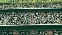 Close-up of railway tracks with wooden sleepers and gravel. Vegetation is visible in the background, adding a touch of greenery.
