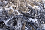 A tangled mass of metallic shavings and spirals, likely from a machining process, is shown with some patches of white snow collected among the metal. The surfaces are shiny and reflect the light, creating a contrast between the cold metallic texture and the soft snow.