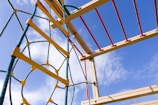 A group of children laughing and climbing on colorful playground equipment under a clear sky.