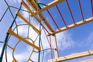 An outdoor jungle gym featuring a climbing structure with colorful ropes and beams against a backdrop of a blue sky with a few clouds.