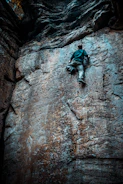 An athlete climbing a steep rock wall during an obstacle race.