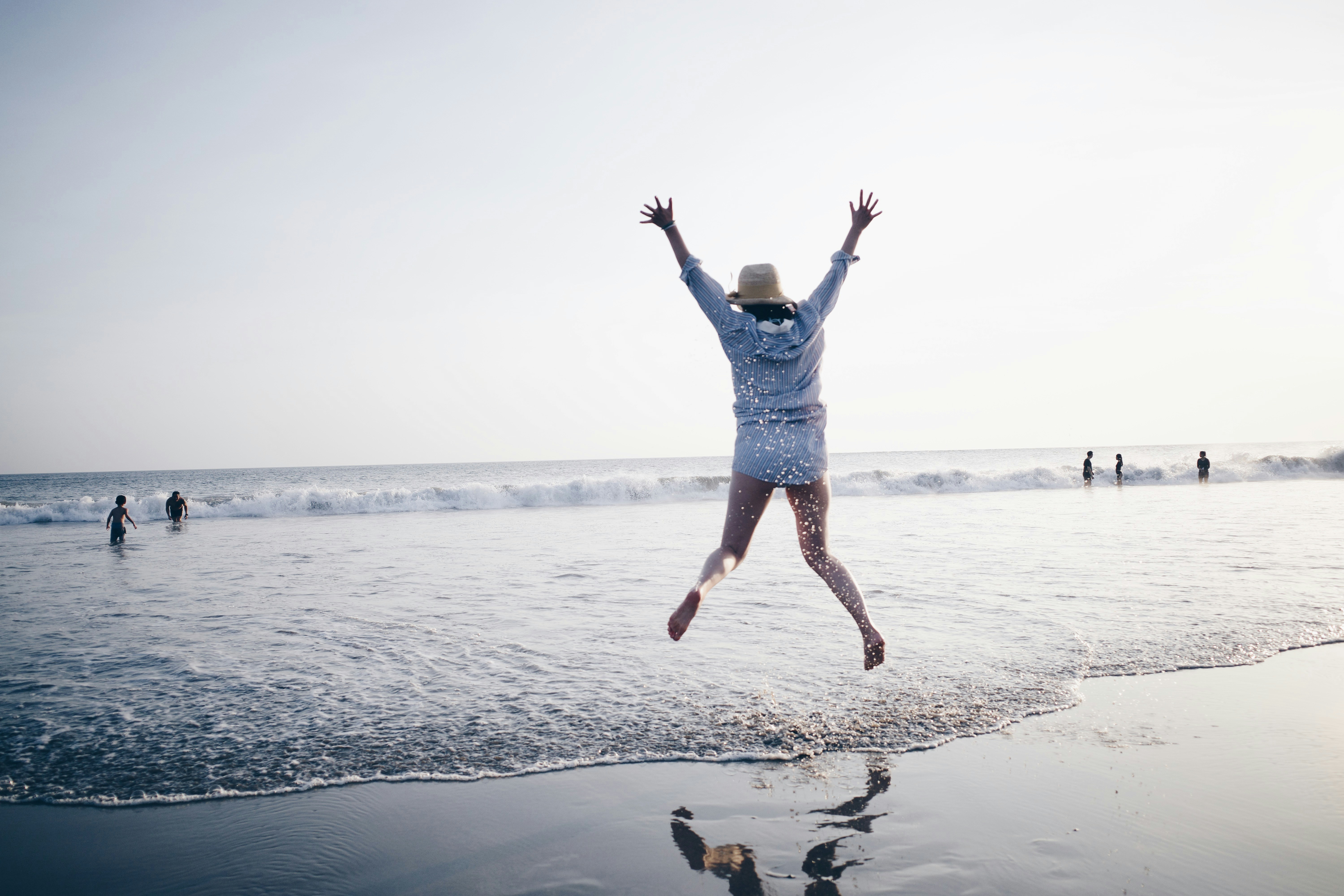 jumping woman wearing hat on seashore
