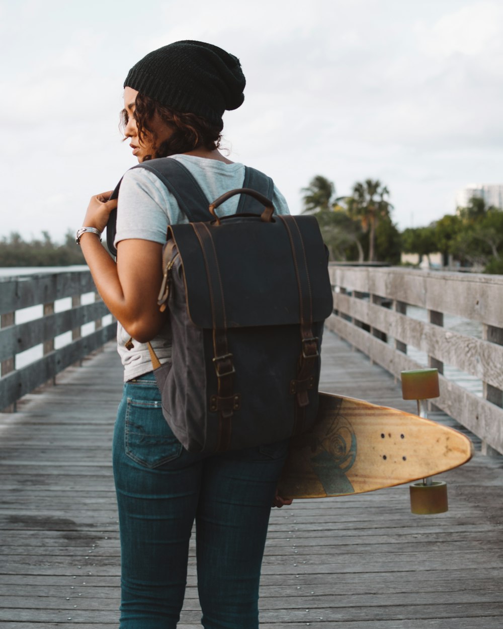 woman carrying gray backpack and long board during daytime