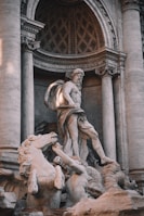 A detailed marble sculpture featuring a mythological scene with a prominent central figure in a classical pose surrounded by horses and other mythological characters set against an intricately carved architectural backdrop.