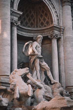 A detailed marble sculpture featuring a mythological scene with a prominent central figure in a classical pose surrounded by horses and other mythological characters set against an intricately carved architectural backdrop.