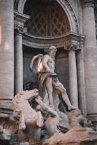 A detailed marble sculpture featuring a mythological scene with a prominent central figure in a classical pose surrounded by horses and other mythological characters set against an intricately carved architectural backdrop.