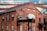 A red brick building with large arched windows and rectangular windows, featuring a sign that reads 'The Foundry'. The structure has a contemporary architectural style with a combination of brick and glass. The upper part of the building includes glass windows reflecting clouds, creating a contrast between the industrial aesthetic and modern elements.