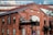 A red brick building with large arched windows and rectangular windows, featuring a sign that reads 'The Foundry'. The structure has a contemporary architectural style with a combination of brick and glass. The upper part of the building includes glass windows reflecting clouds, creating a contrast between the industrial aesthetic and modern elements.