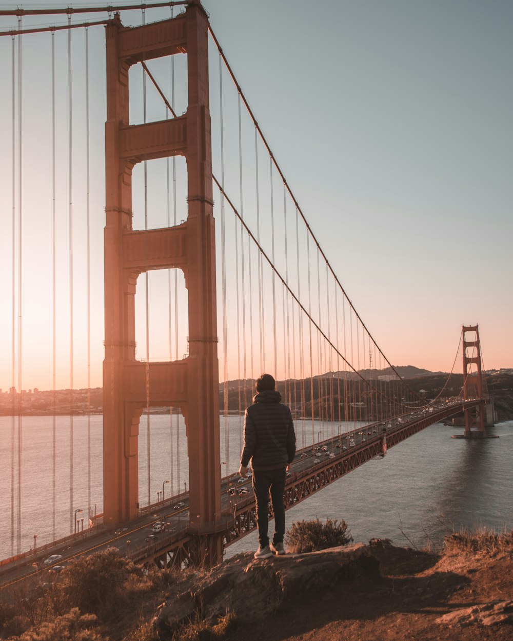 person standing on cliff in front of bridge