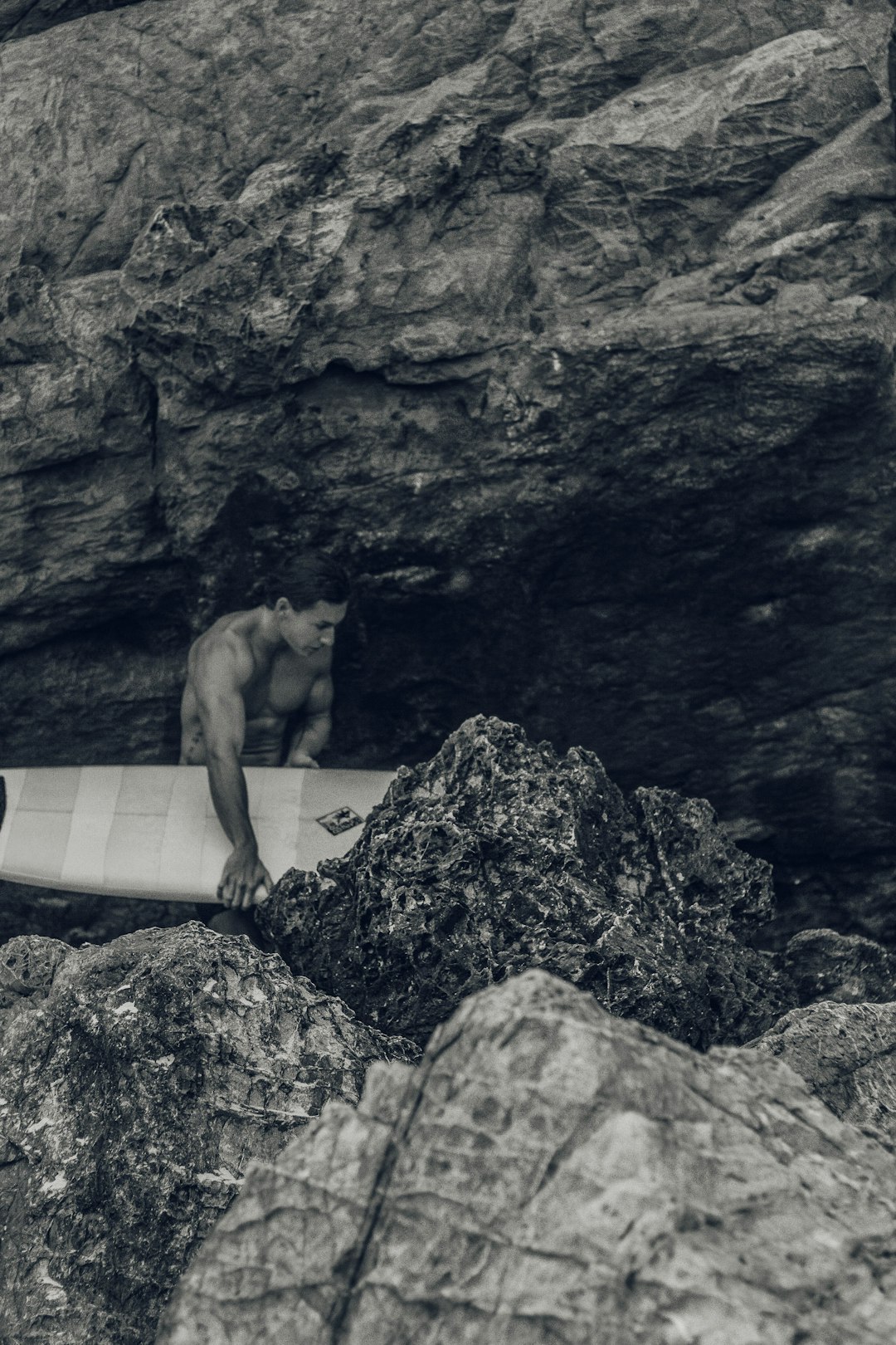 man holding surfboard beside rock