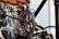 A close-up of a bicycle gear and chain with a person's hand working on it. The focus is on the metal components, showing precise details of the gear and chain mechanism. The background includes blurred out parts of the bicycle and other equipment.