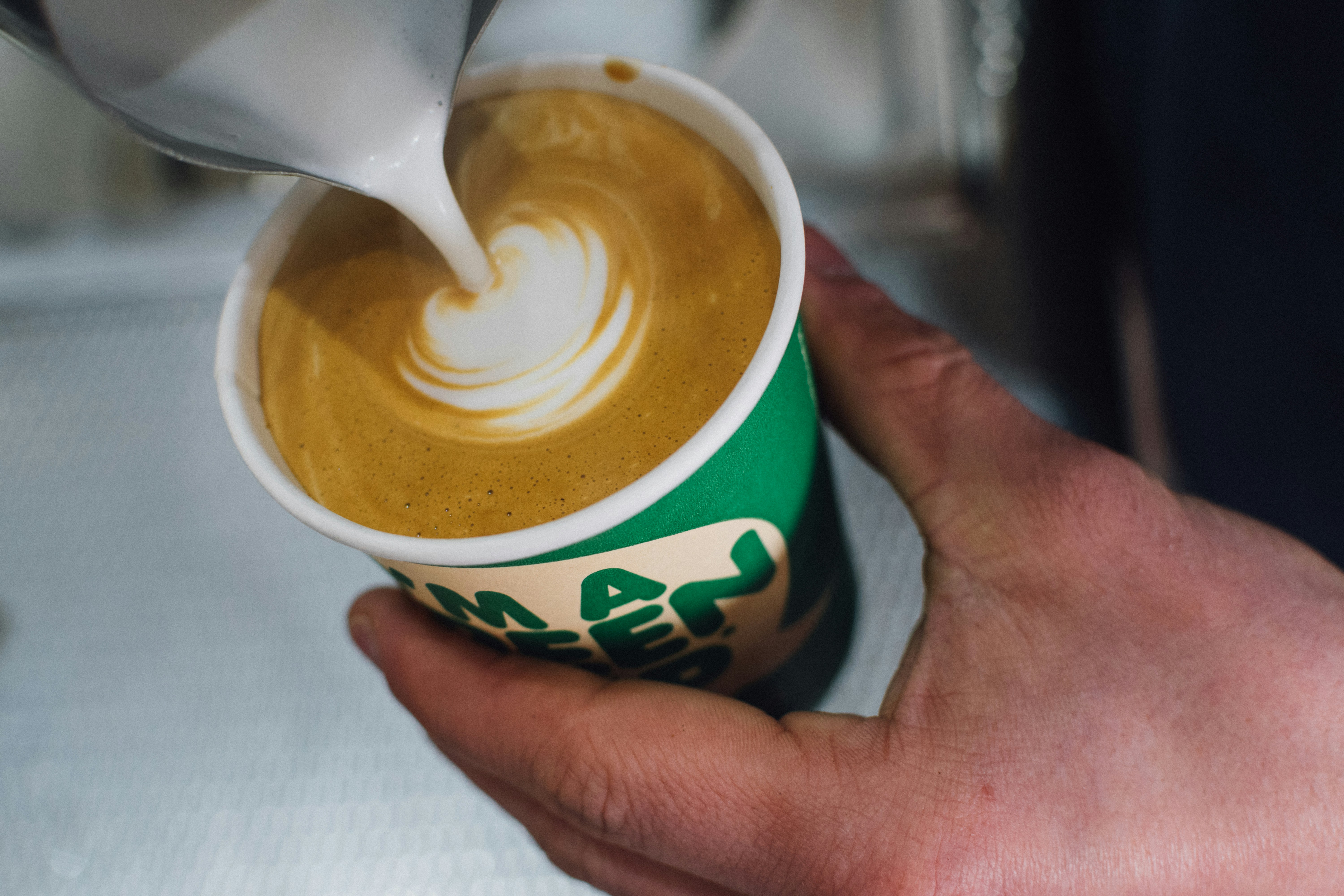 person pouring latte in disposable cup