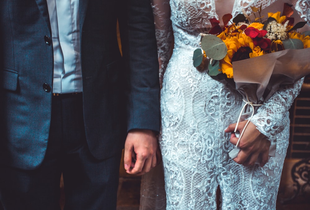 woman in white lace dress and man in suit jacket holding hands