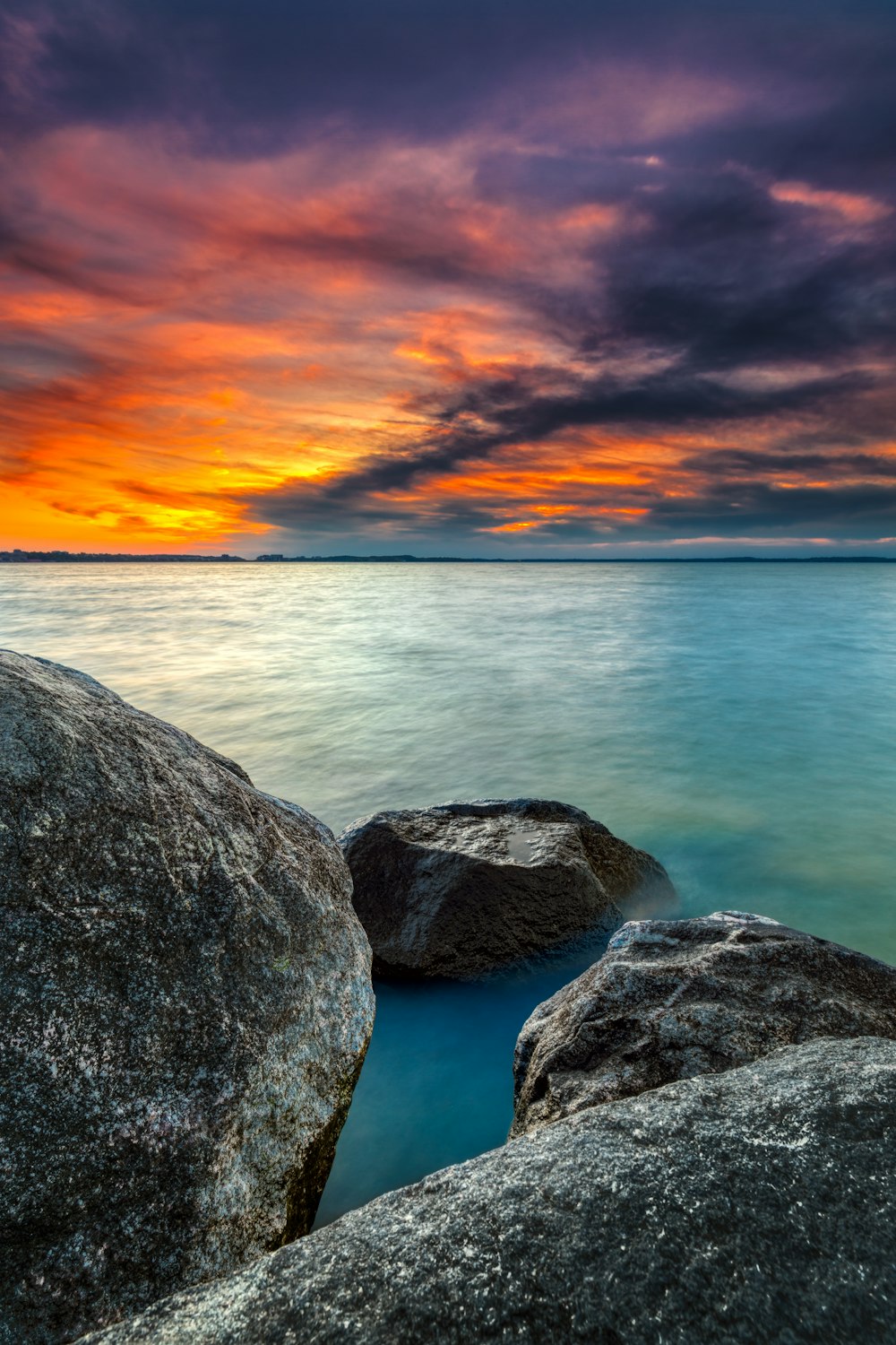 Una puesta de sol sobre un cuerpo de agua con rocas en primer plano