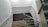 A staircase with a modern design features glass panels and metallic railings. The steps are covered with a dark carpet in a pattern, and the walls are painted white, creating a clean and minimalist appearance.