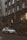 A silver luxury SUV is parked on a city street in front of a Gucci store. The building facade is ornate with large arched windows and decorative elements, including sculptures. The scene is urban, with greenery on the sidewalk and warm lights illuminating the storefront.