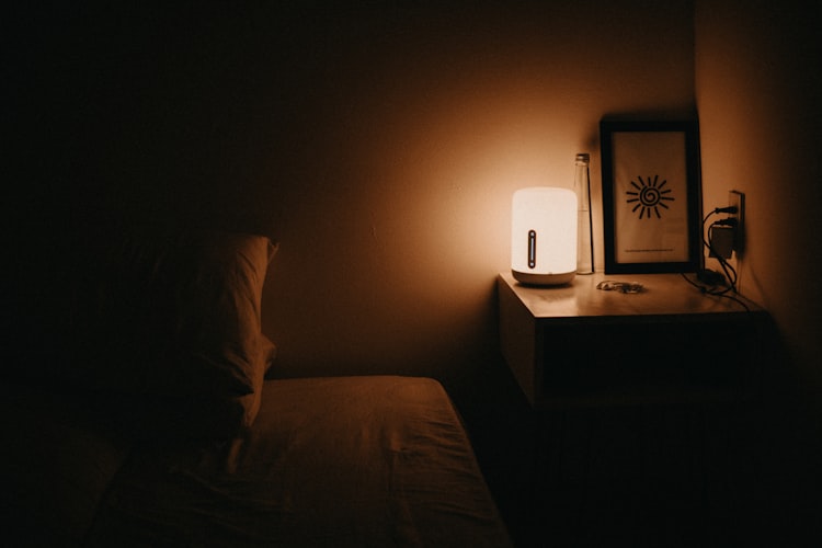 A bedroom in darkness except for a small bedside table lamp