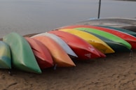 A collection of colorful kayaks lined up on a rocky lakeside beach.