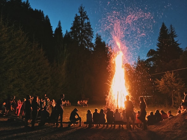 Community members gathered around a bonfire at dusk with a fox silhouette in the background.