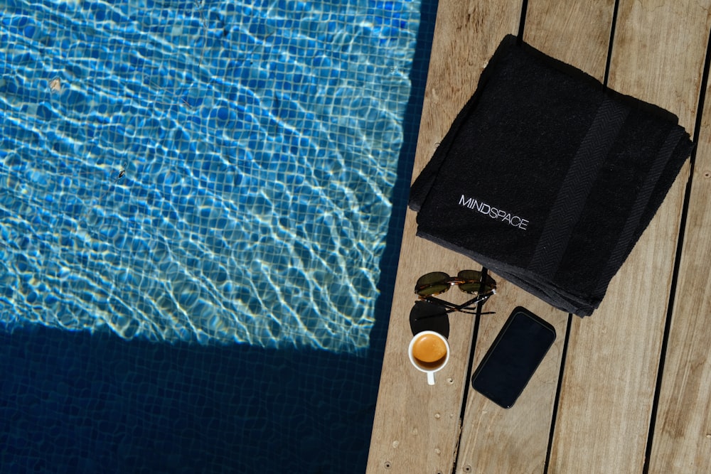 a towel, sunglasses, and a cup of coffee on a wooden table next to