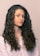 A person with long, curly brown hair wearing a light-colored shirt is looking slightly to the side. The hair is voluminous and well-defined, cascading down the shoulders.