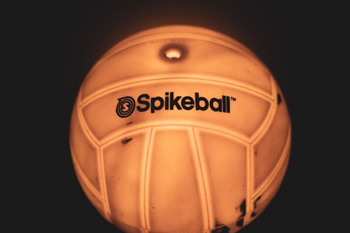 A close-up view of a ball with the logo 'Spikeball' visible on its surface. The ball appears to be illuminated with a warm, yellow-orange glow, accentuating its texture and design.