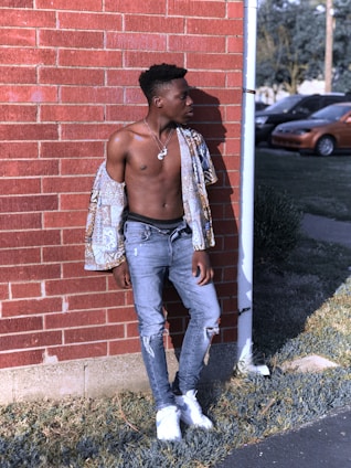 A stylish man in casual jeans and a jacket standing against a brick wall