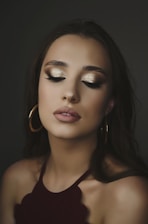 woman in maroon halter top, gold-colored hoop earrings, and gold eyeshadow